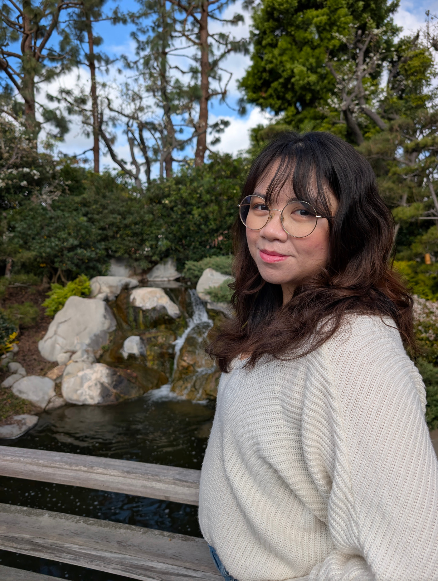 Sam smiling beside a waterfall in a garden